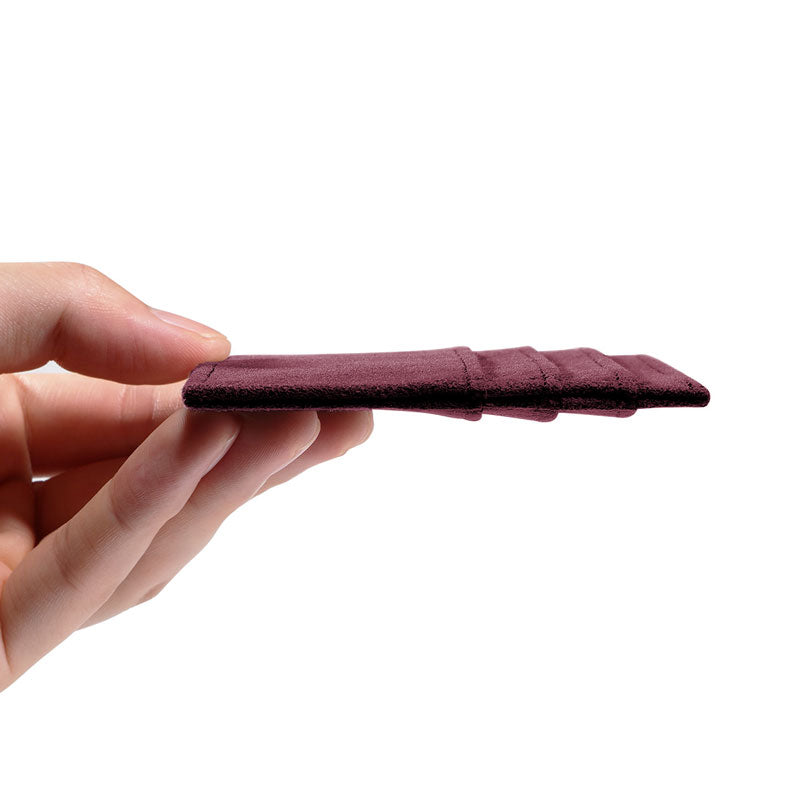 Burgundy Alcantara card wallet, side view held flat in one hand to show the slim profile, on a plain white background