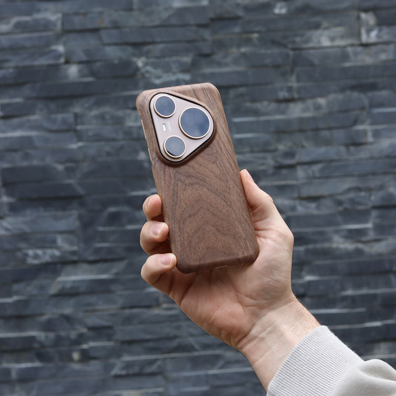 Hand holding a wooden phone case for Huawei Pura 80 Ultra in walnut against a stone wall background