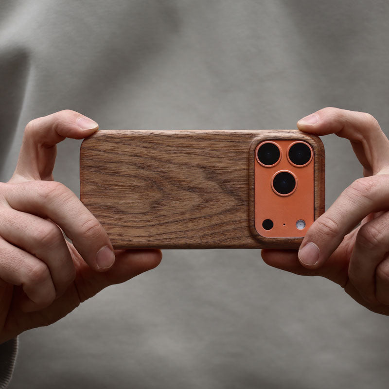 Komodoty Slim Wood iPhone Case on an iPhone 17 Pro Orange held by man hands against his khaki jumper