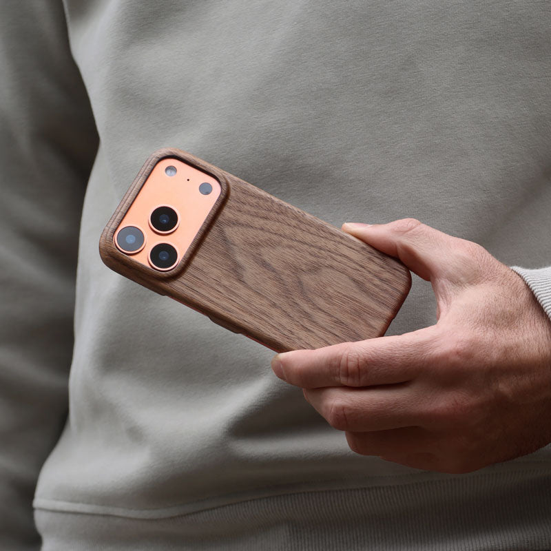 Man holding a Komodoty Slim Wood iPhone Case on an iPhone 17 Pro Orange held by man's hand upside down against his khaki colored sweater as the background
