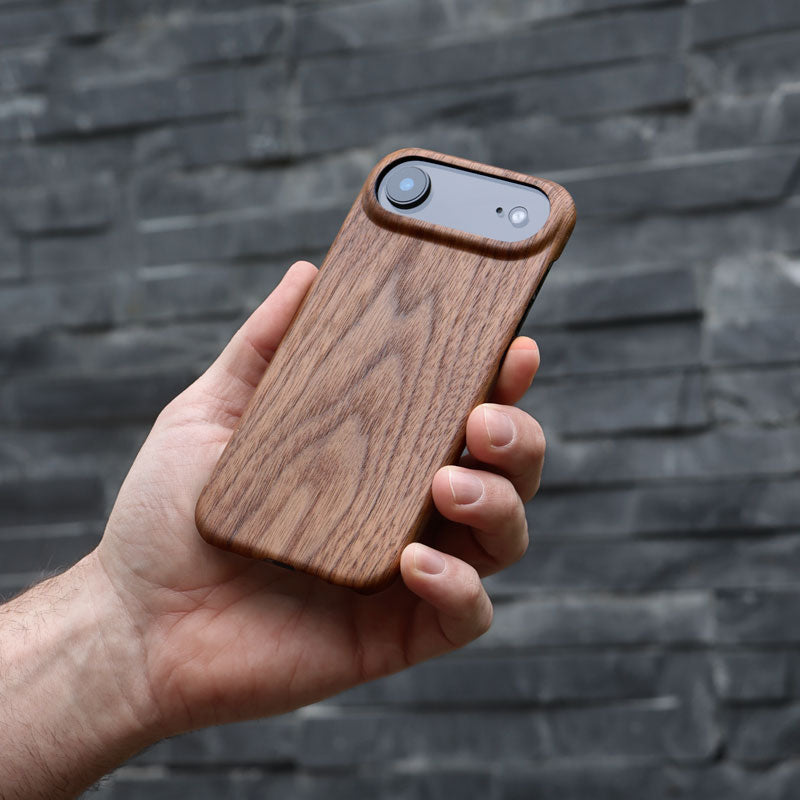 Hand holding a Komodoty Slim wooden iPhone Air case against a stone wall background