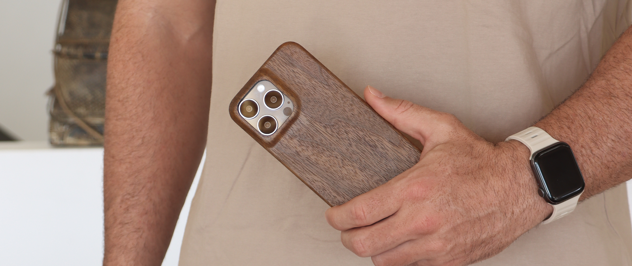 Komodoty Komodo Man holding Slim Wood Phone Case iPhone 15 Pro Max Walnut case with bumper watch band and beige shirt desktop banner 2200 x 920