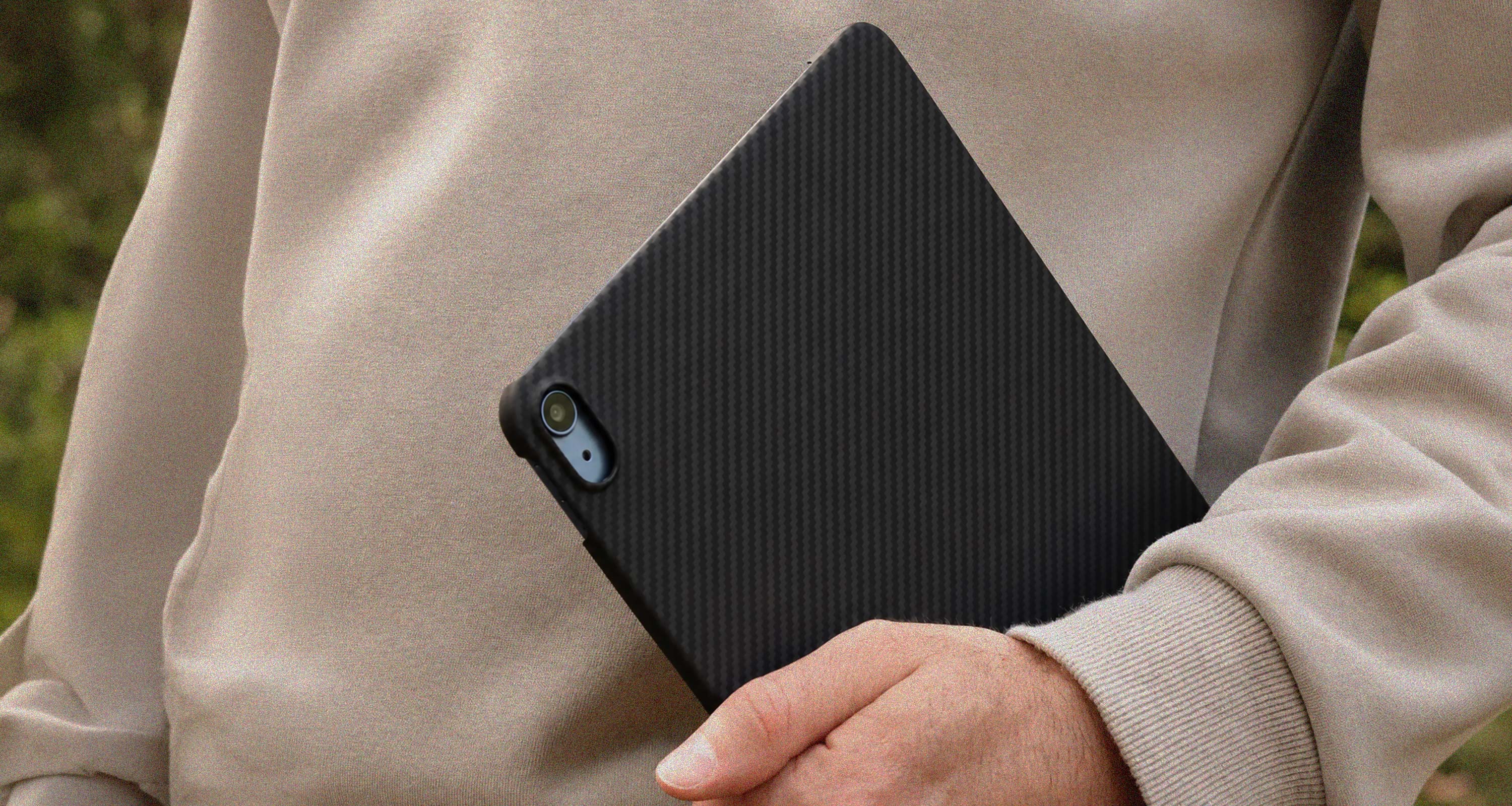 Person holding a black aramid fiber kevlar ipad case against a blurred natural background