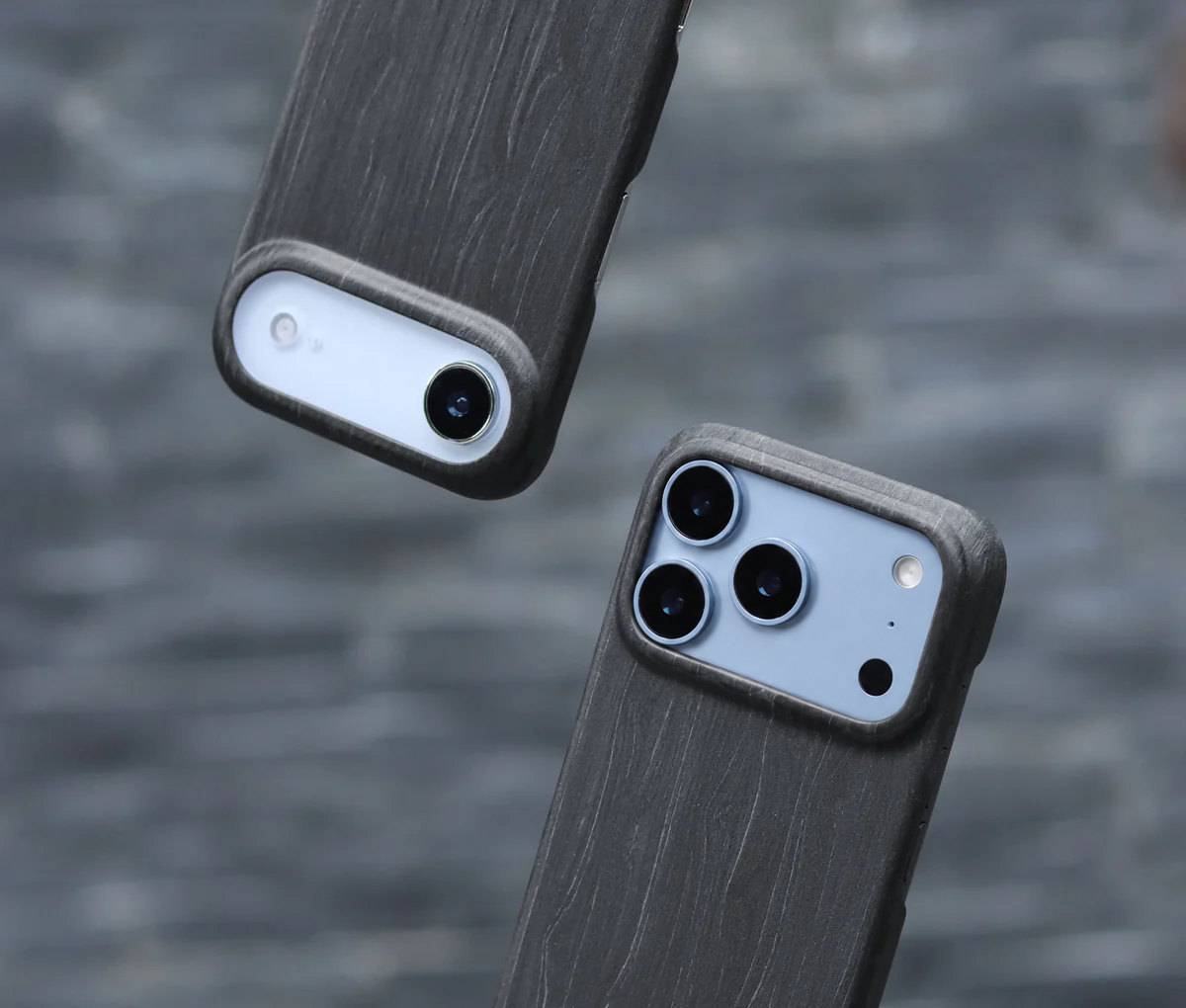 Two dark gray wood-grain textured iPhone Air white on the left and the iPhone 18 Pro Max in glacier light blue on the right with charcoal wooden phone cases shown from the back, one with a single camera cutout and one with a triple-camera cutout, set against a blurred gray background.